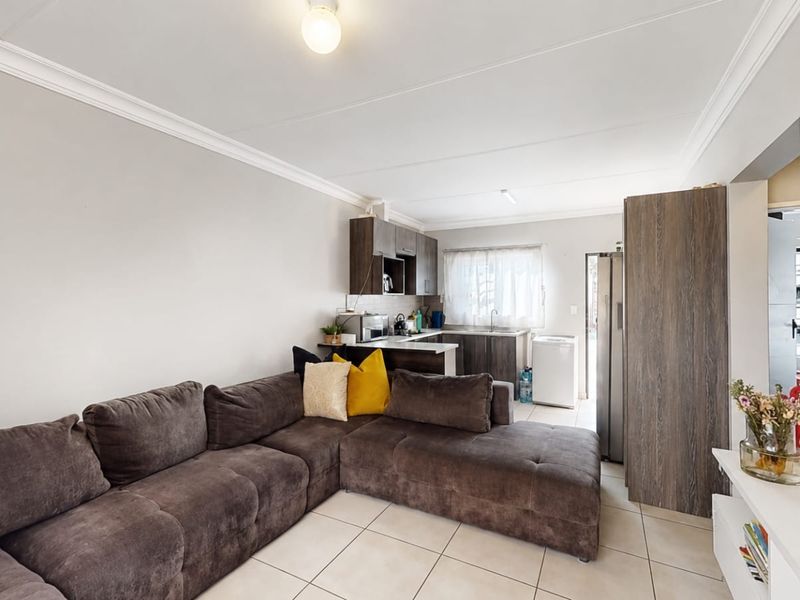 Open-plan living area featuring tiled flooring, ceiling cornices, and a compact kitchen with built-in cabinetry and sink.