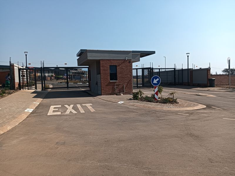 A modern residential estate entrance featuring a brick security gatehouse, automated access gates, electric fencing, and paved driveway infrastructure.