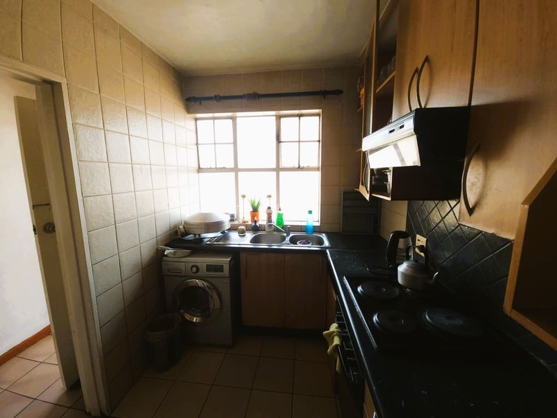 A compact, dated kitchen featuring built-in cabinetry, a double sink, an electric hob with an extractor fan, and tiled finishes throughout.