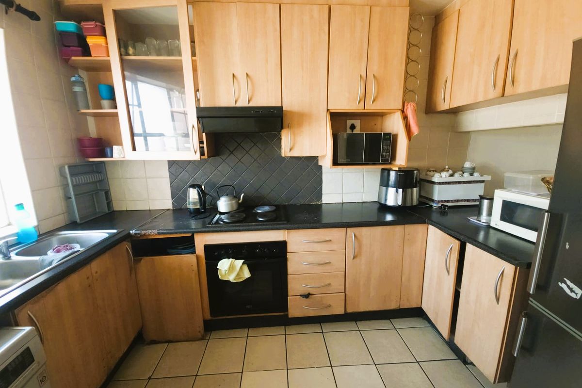 A functional kitchen featuring light wood-tone cabinetry, black laminate countertops, a built-in oven with hob, and tiled flooring.