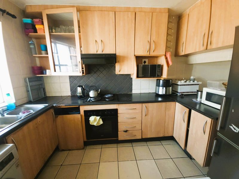 A functional kitchen featuring light wood-tone cabinetry, black laminate countertops, a built-in oven with hob, and tiled flooring.