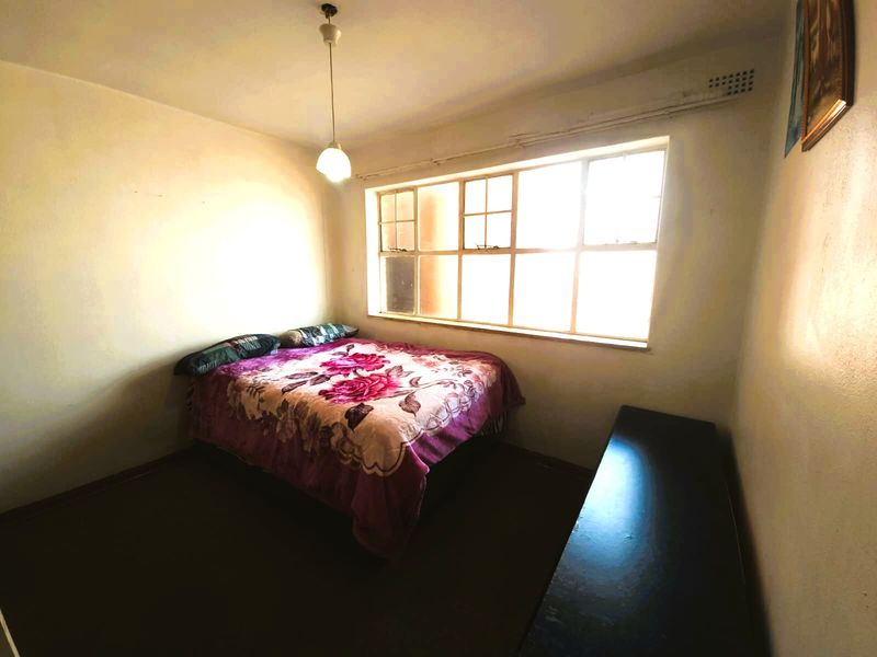 A bedroom featuring a large multi-pane window providing natural light, with a simple pendant light fixture and basic interior finishes.