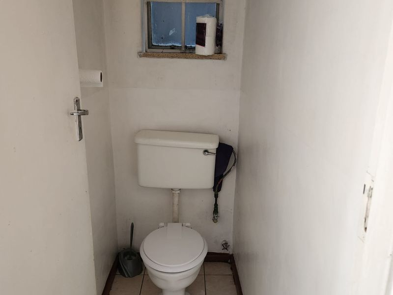 A compact, functional guest toilet featuring ceramic floor tiles and a small window, currently in need of cosmetic updates and maintenance.