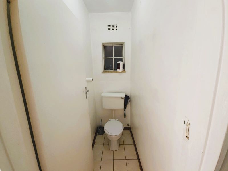 A compact, functional guest toilet featuring tiled flooring and a small ventilation window.
