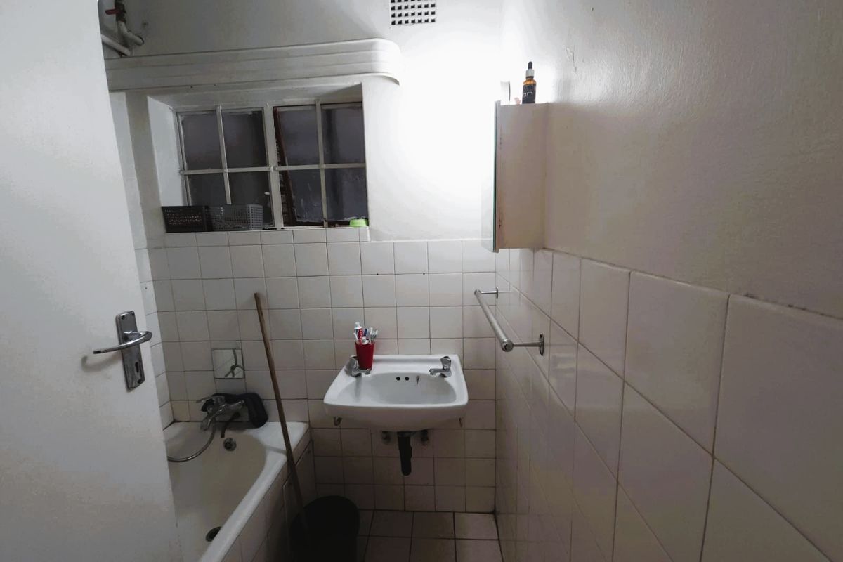 A compact bathroom featuring a wall-mounted basin, bathtub, and tiled finishes, requiring cosmetic updates to improve its overall condition and appeal.