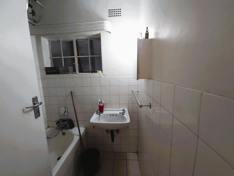 A compact bathroom featuring a wall-mounted basin, bathtub, and tiled finishes, requiring cosmetic updates to improve its overall condition and appeal.