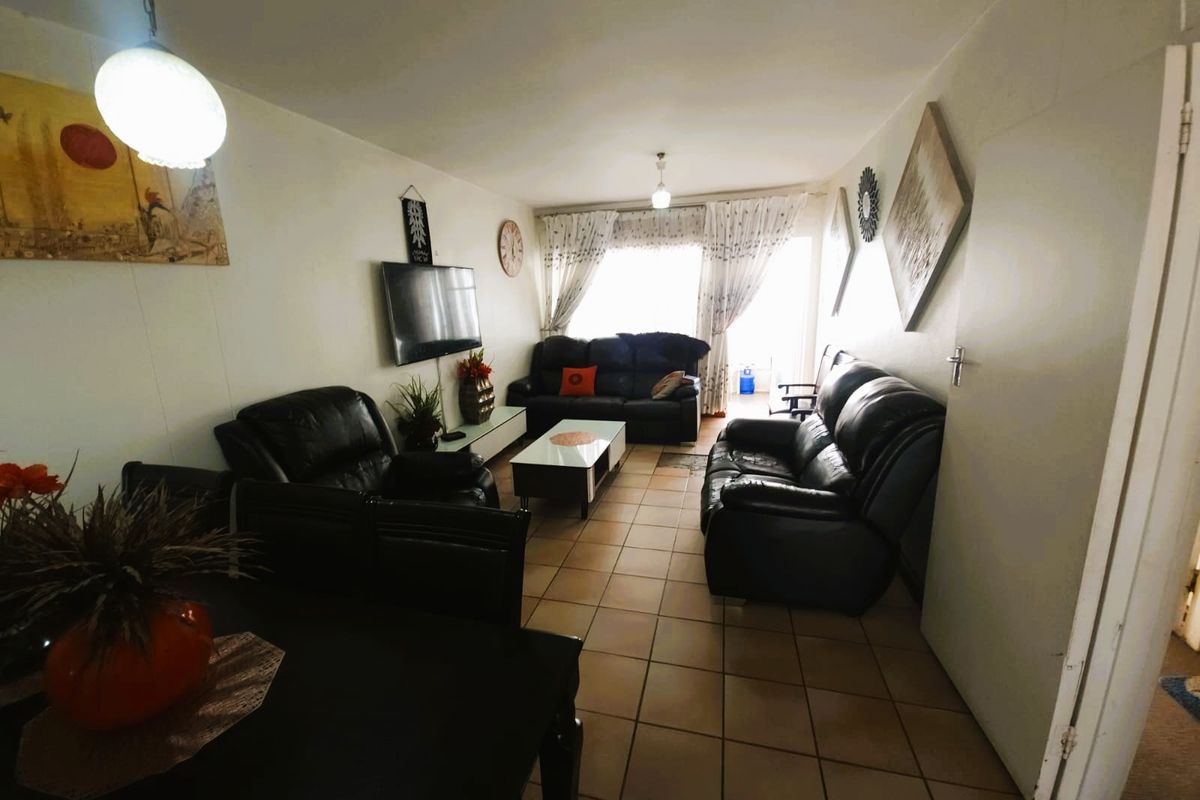 A spacious living room featuring tiled flooring, neutral walls, and a sliding glass door providing access to the outdoor area.