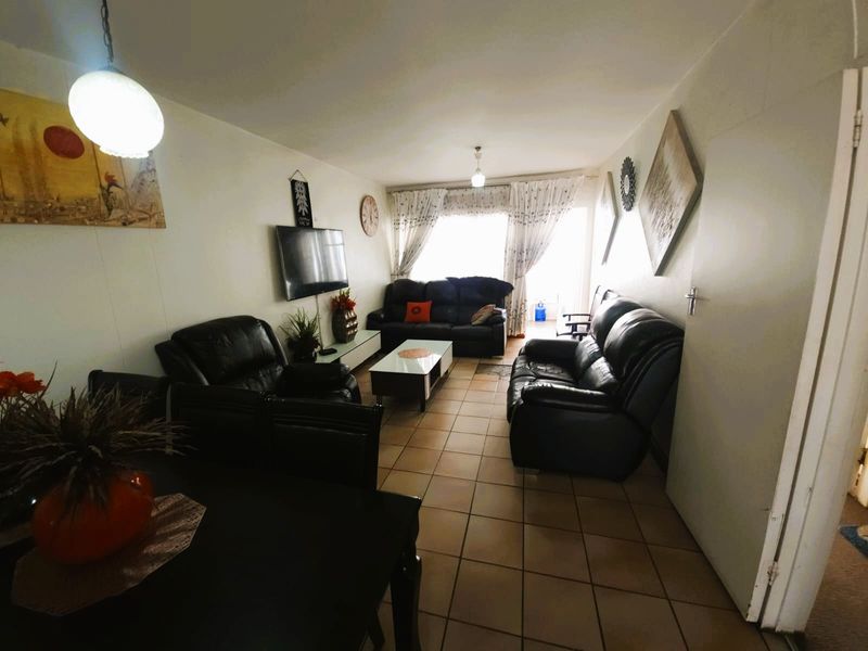 A spacious living room featuring tiled flooring, neutral walls, and a sliding glass door providing access to the outdoor area.