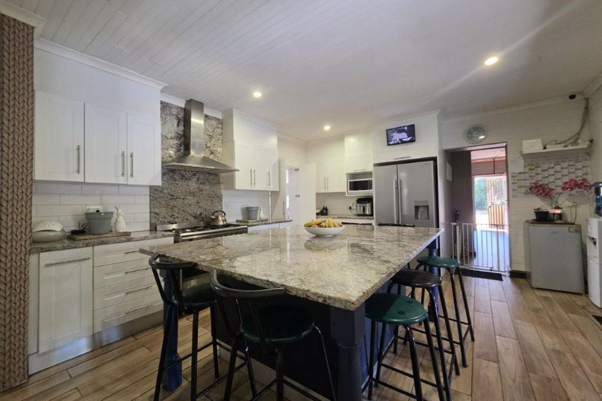 Modern kitchen featuring a large granite-topped island, shaker-style cabinetry, stainless steel appliances, and wood-look tile flooring.
