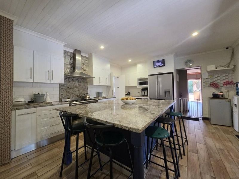 Modern kitchen featuring a large granite-topped island, shaker-style cabinetry, stainless steel appliances, and wood-look tile flooring.