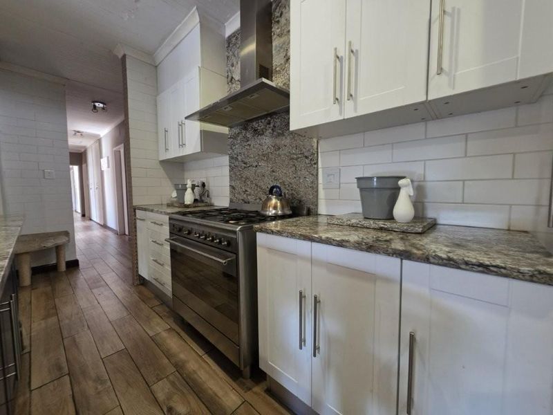 Modern kitchen featuring white shaker cabinetry, granite countertops, subway tile backsplash, and a stainless steel gas stove with extractor fan.