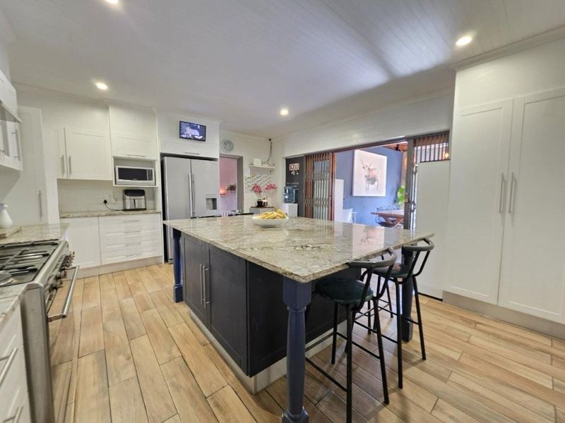 Modern kitchen featuring a large granite-topped island, gas range stove, ample built-in cabinetry, and timber-look floor tiles with seamless access to the outdoor area.