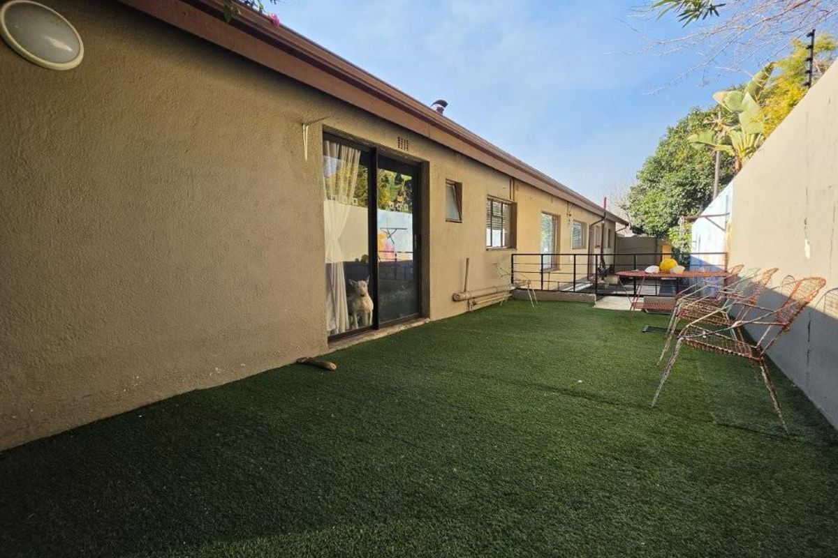 Rear exterior view of the property featuring a paved area with artificial turf, sliding door access, and boundary walling.