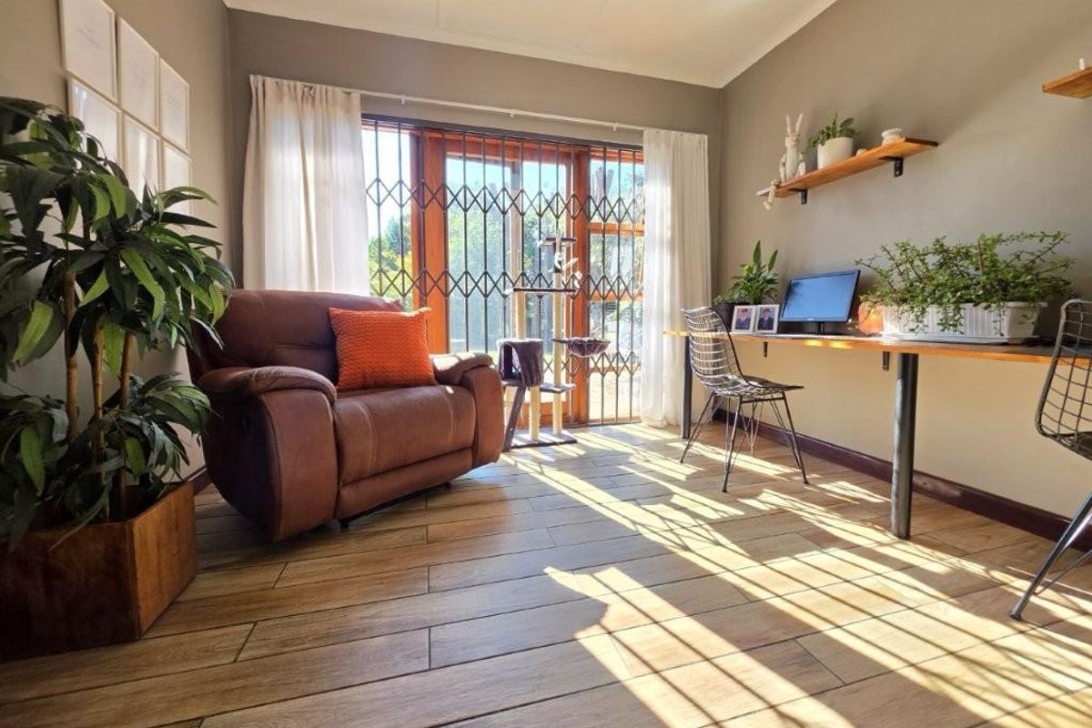 A bright living area featuring wood-look tile flooring, a timber-framed sliding door with security gate, and a built-in floating wall shelf.