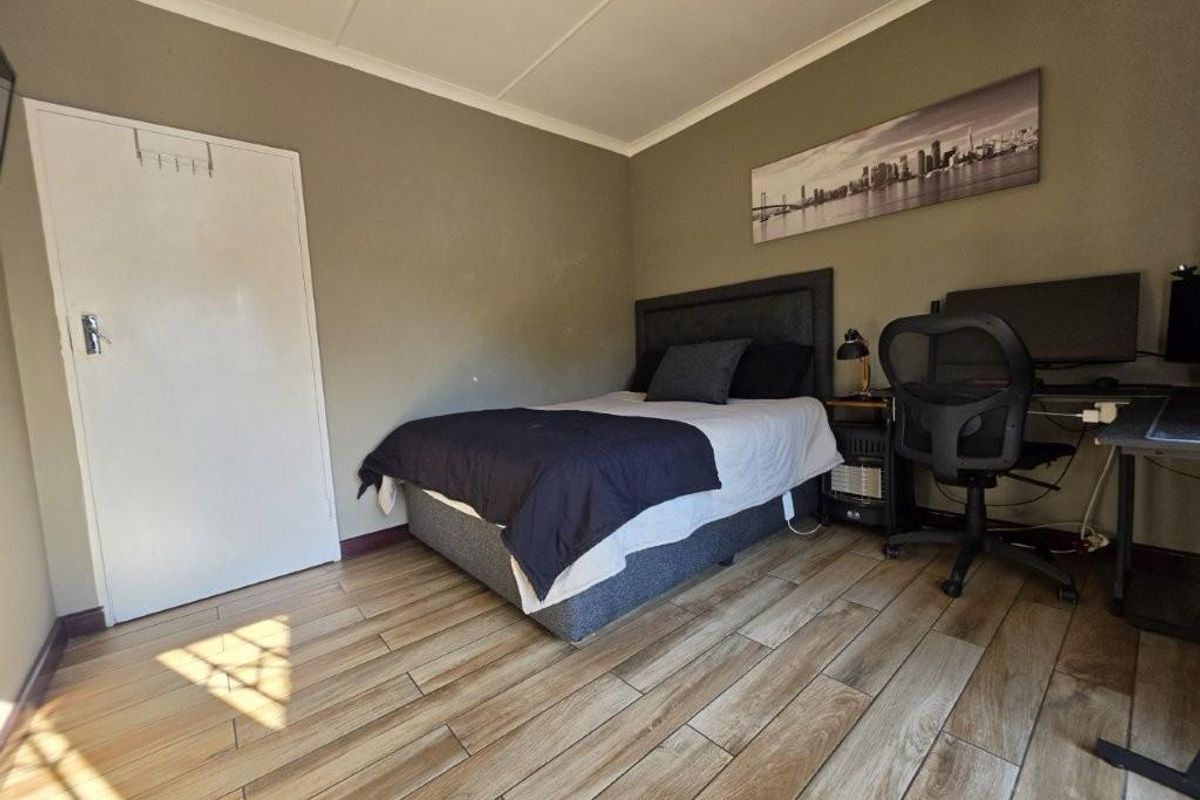 A functional bedroom featuring wood-look tiled flooring and neutral wall tones, providing a clean and practical living space.