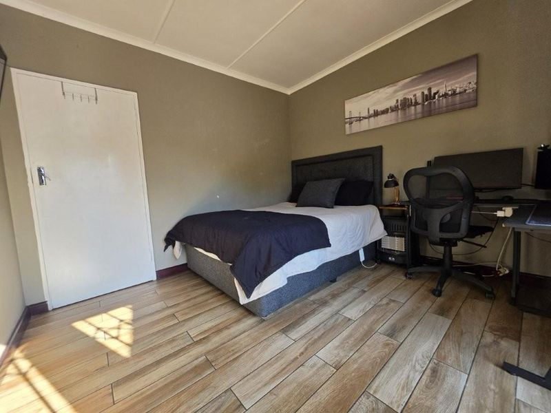 A functional bedroom featuring wood-look tiled flooring and neutral wall tones, providing a clean and practical living space.