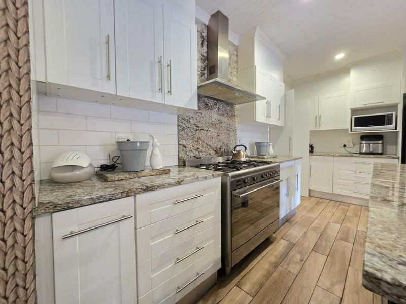 Modern kitchen featuring white shaker cabinetry, granite countertops, subway tile backsplash, and stainless steel appliances including a gas stove and extractor fan.