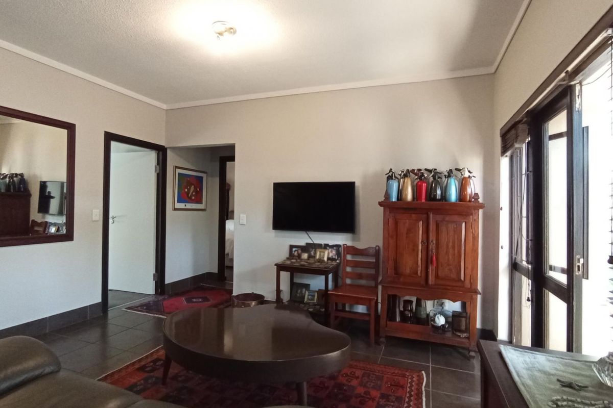 A living room featuring tiled flooring, neutral walls, and sliding glass doors with venetian blinds, providing access to an adjacent area.
