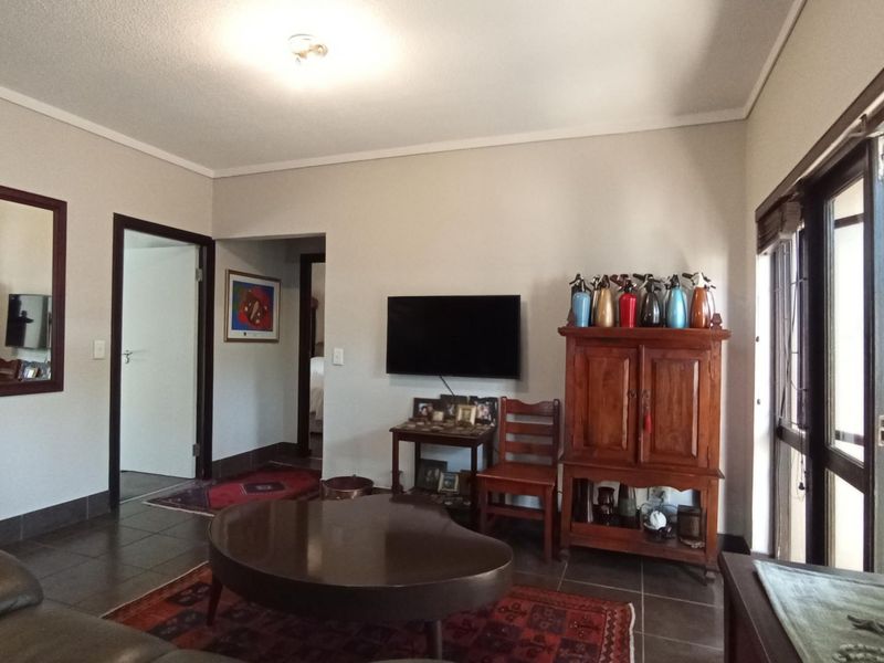 A living room featuring tiled flooring, neutral walls, and sliding glass doors with venetian blinds, providing access to an adjacent area.