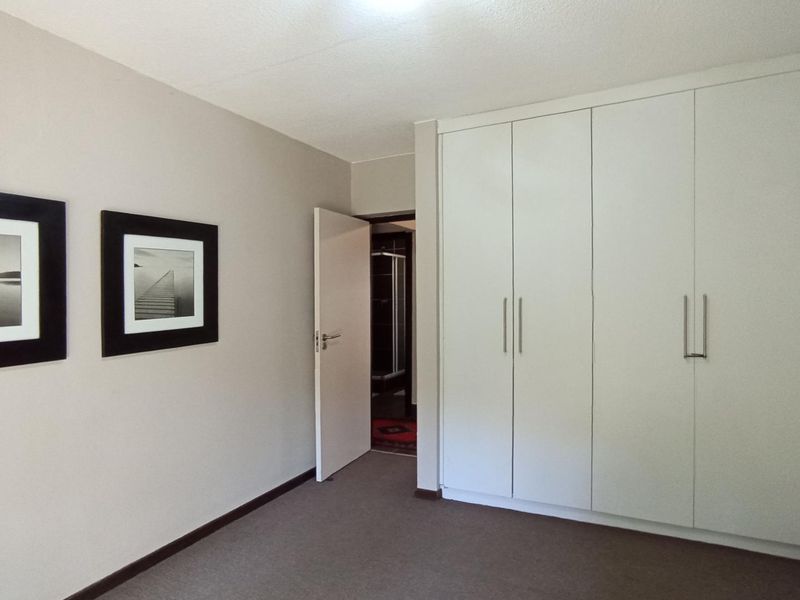 A clean, neutral bedroom featuring built-in cupboards and carpeted flooring, offering a versatile space with direct access to an adjoining room.