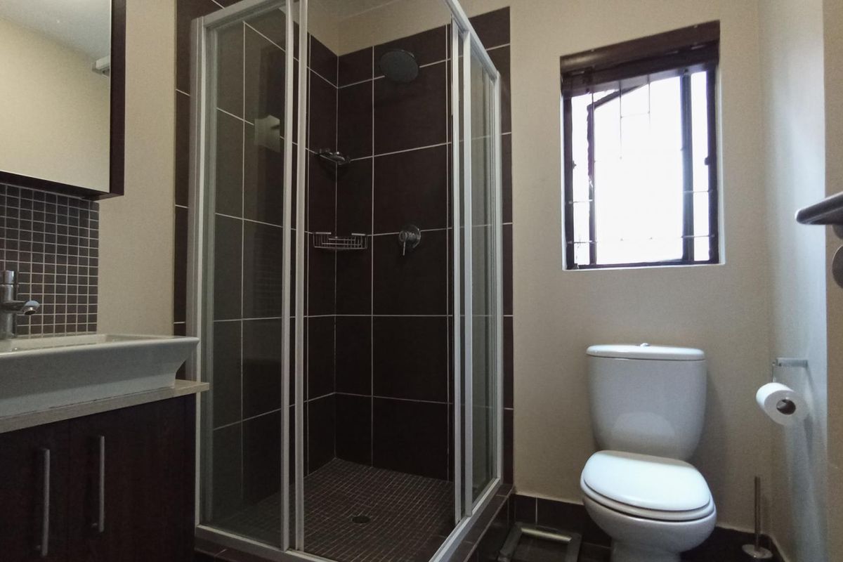 A functional bathroom featuring a shower enclosure, vanity basin, and toilet with dark tiled accents and a window for natural light.