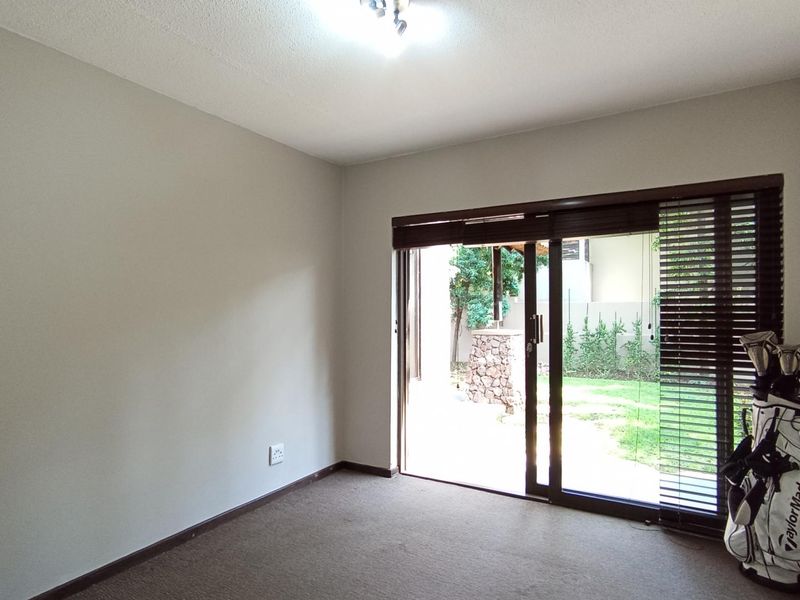A bright, empty bedroom featuring neutral walls, carpeted flooring, and a sliding glass door that provides direct access to the garden area.