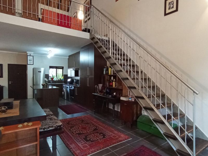 Open-plan living area featuring a modern staircase with metal balustrade, mezzanine level, and integrated kitchen cabinetry with tiled flooring.
