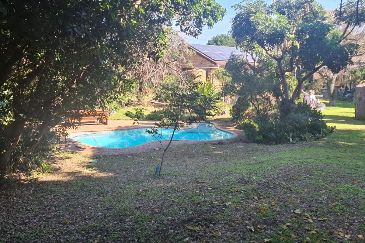 A private backyard featuring a swimming pool, mature trees, and a water storage tank, set within a residential garden space.