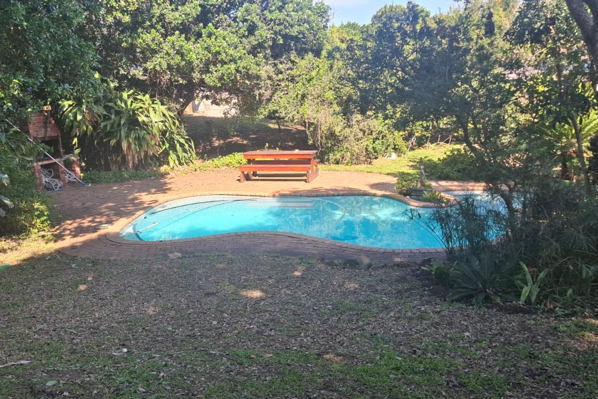 A private swimming pool area featuring brick paving and a built-in braai, surrounded by established garden greenery.