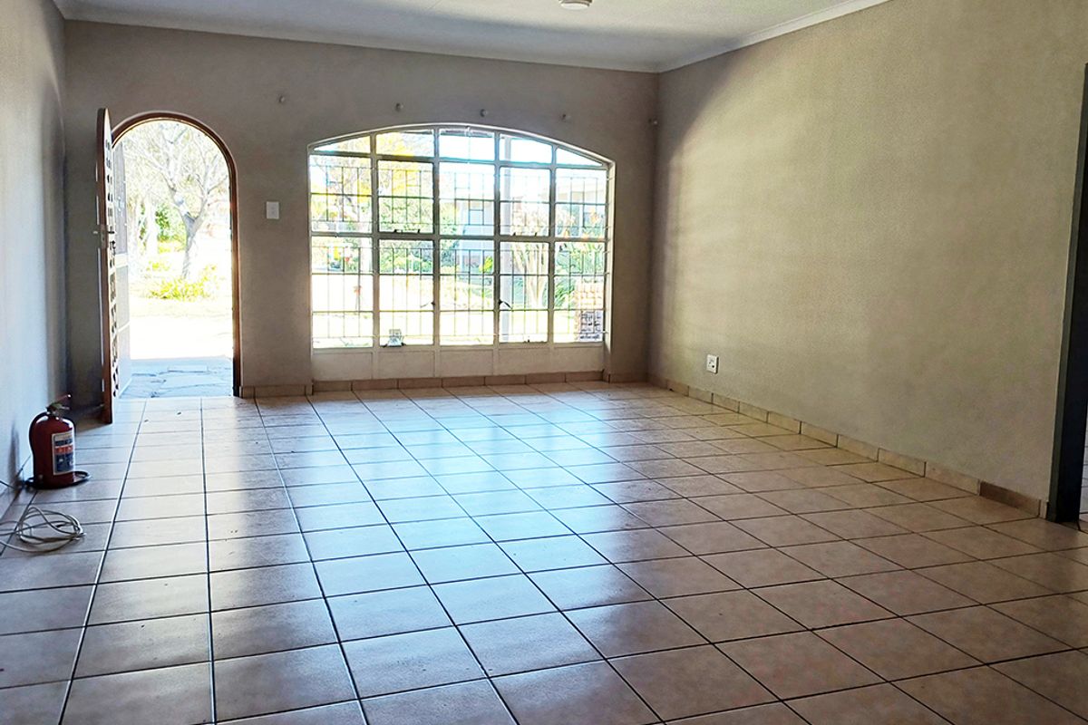 A spacious, empty living area featuring neutral tiled flooring, an arched entrance, and a large arched window providing natural light and garden views.