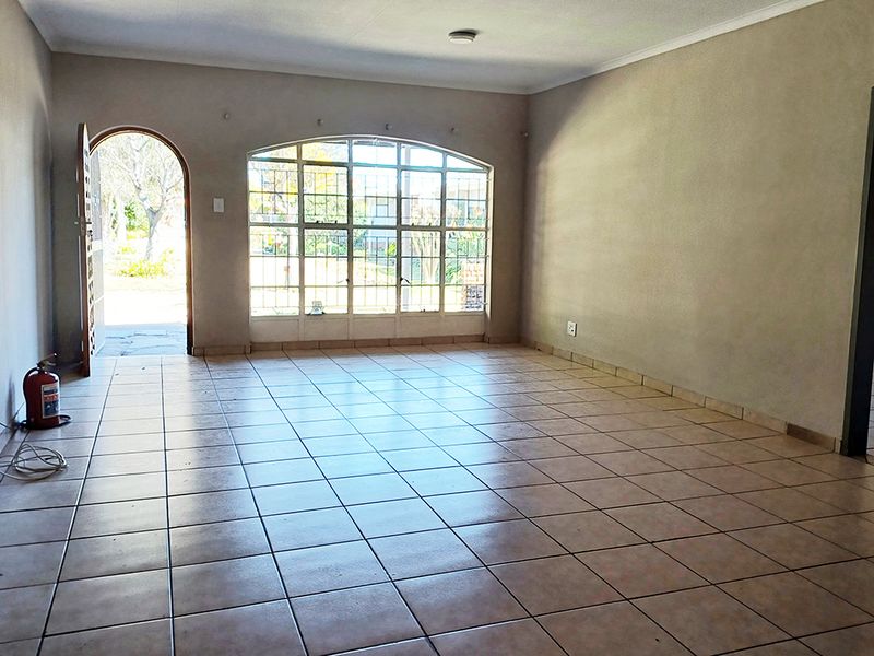A spacious, empty living area featuring neutral tiled flooring, an arched entrance, and a large arched window providing natural light and garden views.