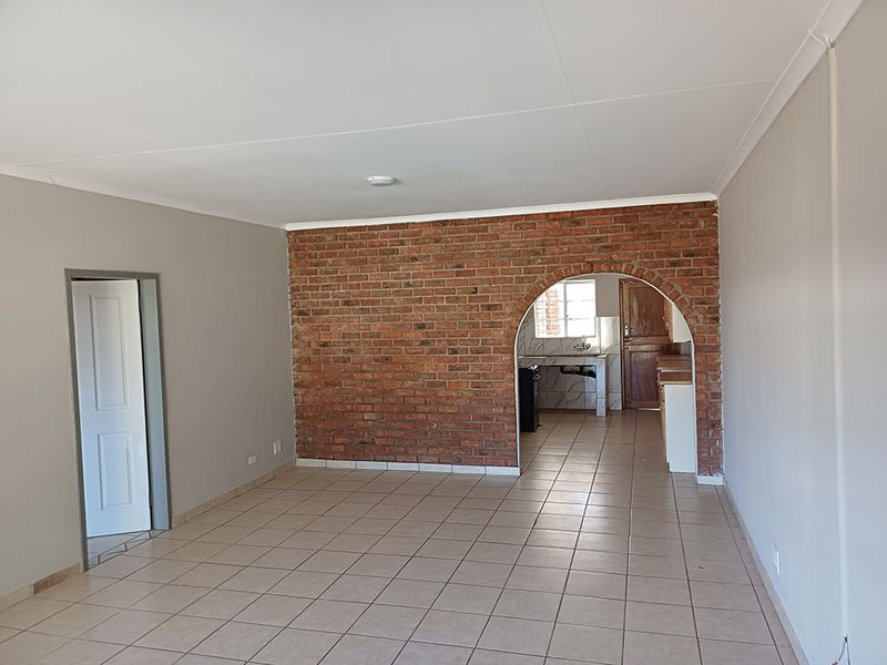 Open plan living area featuring an exposed brick wall with an arched entryway leading into a functional kitchen space with tiled flooring throughout.
