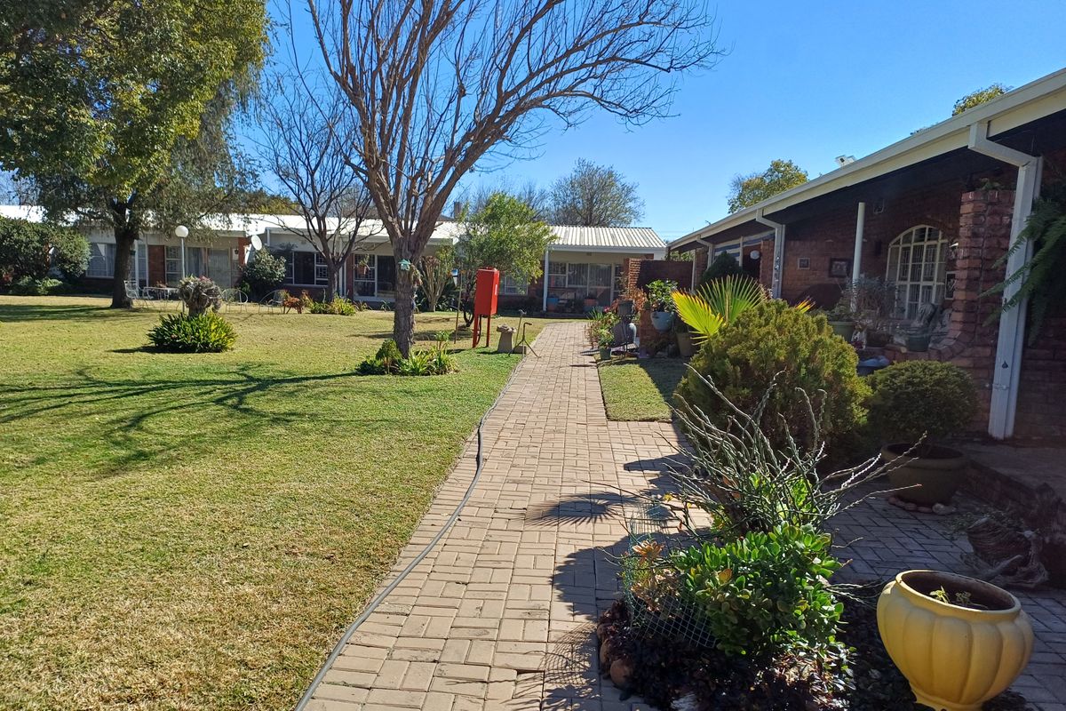 A well-maintained communal garden area featuring a brick paved walkway leading between retirement village units with established landscaping and mature trees.