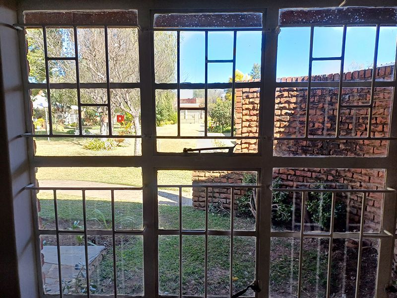 View through a window with security bars looking out onto a landscaped garden and brick boundary wall.
