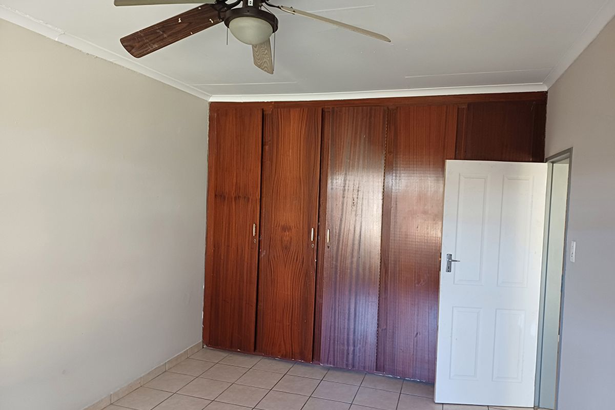 A vacant bedroom featuring built-in wooden cupboards, tiled flooring, and a ceiling fan, offering a neutral space ready for personalization.