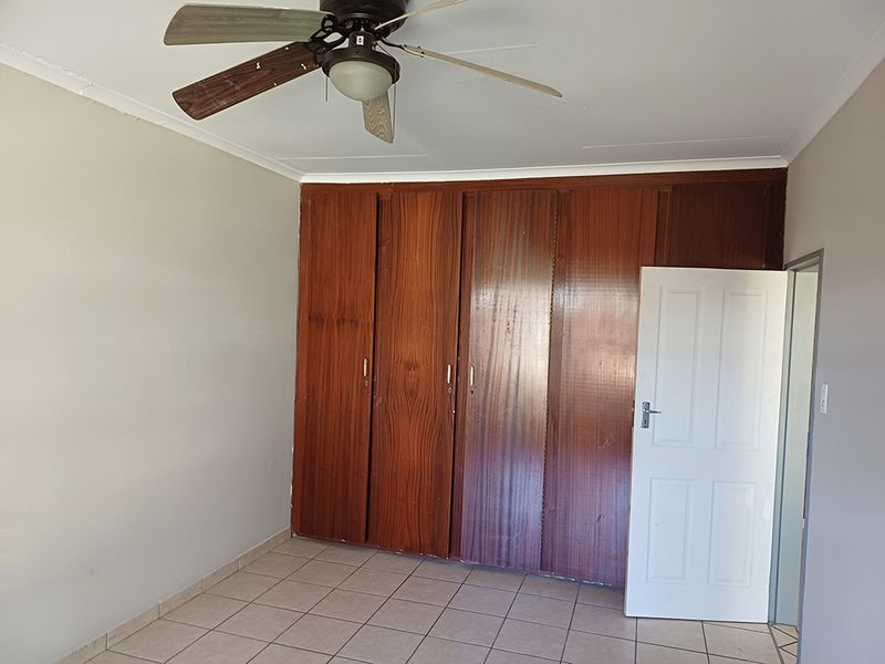 A vacant bedroom featuring built-in wooden cupboards, tiled flooring, and a ceiling fan, offering a neutral space ready for personalization.
