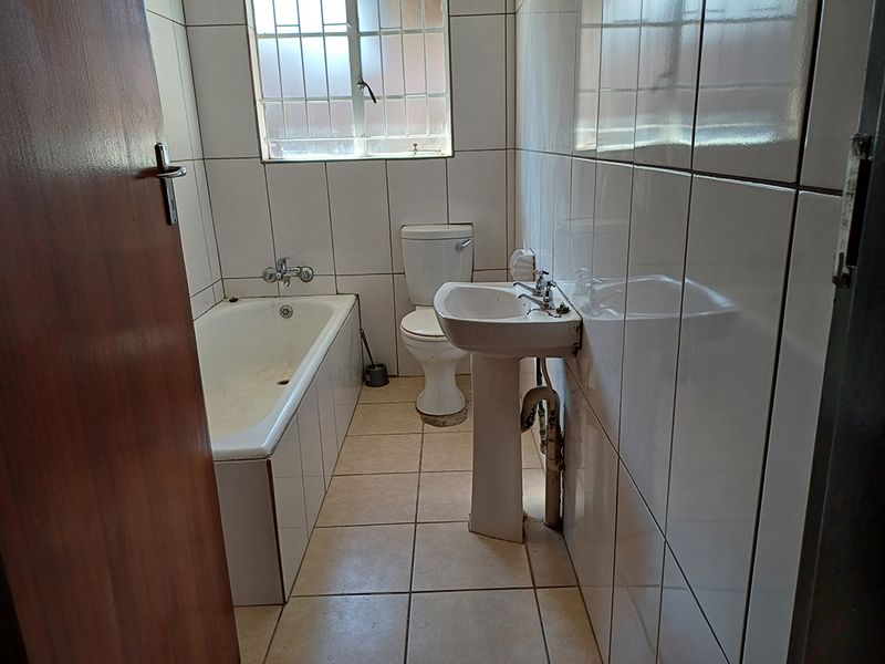 A dated bathroom featuring a standard bathtub, pedestal washbasin, and toilet with full-height ceramic wall tiling and tiled flooring.