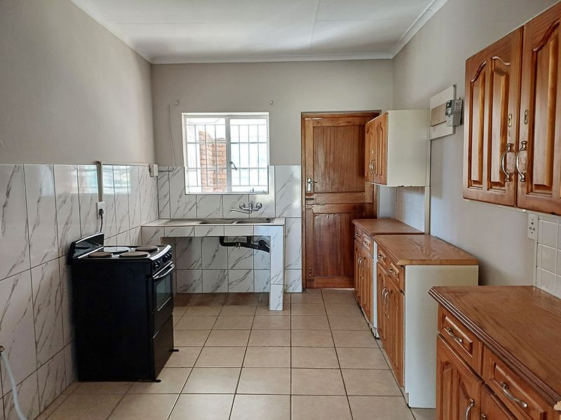 A functional kitchen featuring tiled splashbacks, wooden cabinetry, tiled flooring, and a window with security bars, offering a clean and practical layout.