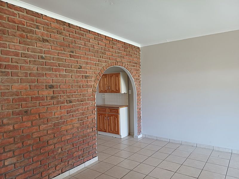 An open-plan living area featuring a distinctive exposed brick wall with an arched opening leading to a compact kitchen with built-in cabinetry.