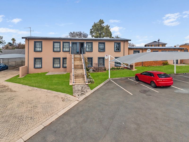 Front elevation of a two-story townhouse complex featuring a paved driveway, shade cloth parking, and an external staircase leading to the upper level.