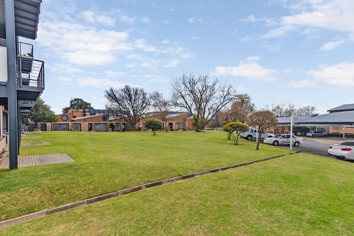 A view of the townhouse complex exterior featuring a large communal lawn, paved patio areas, and covered parking bays.
