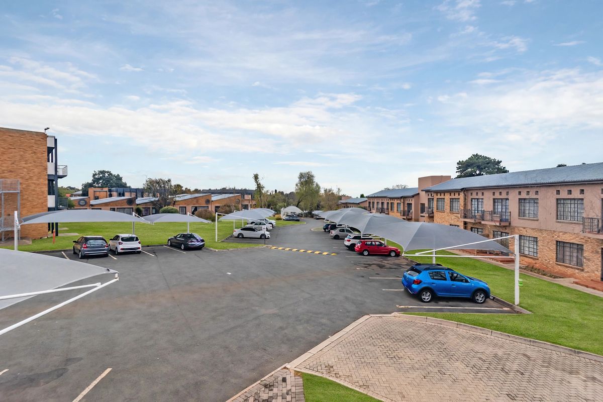 An elevated view of the townhouse complex parking area featuring multiple shade cloth carports, paved pathways, and well-maintained communal lawn spaces.