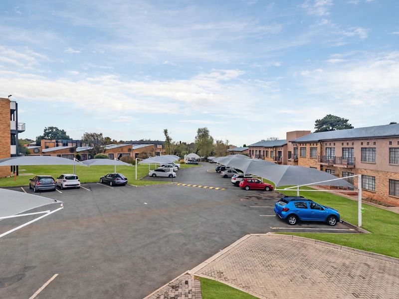 An elevated view of the townhouse complex parking area featuring multiple shade cloth carports, paved pathways, and well-maintained communal lawn spaces.