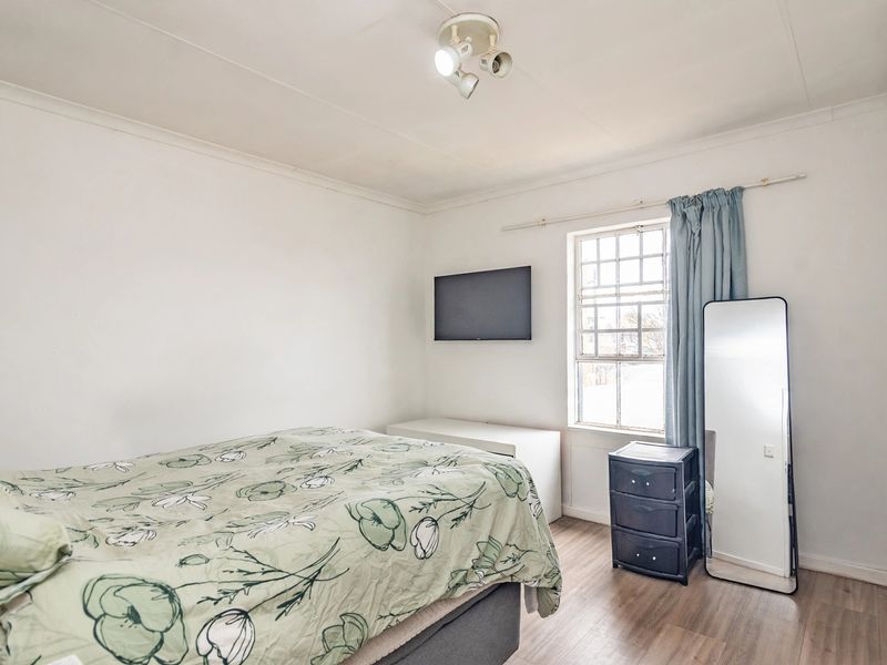 A functional bedroom featuring laminate flooring, a multi-pane window, and a ceiling-mounted spotlight fixture.