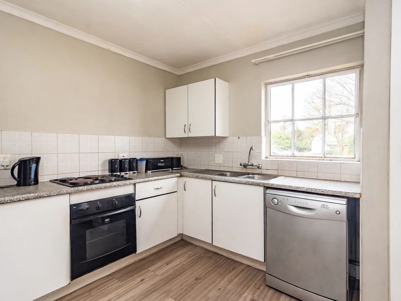 A functional kitchen featuring built-in cabinetry, a tiled splashback, electric hob, oven, and a double sink with a window view.