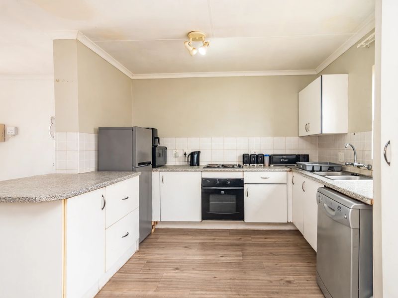 A functional kitchen featuring laminate countertops, built-in oven and hob, tiled backsplash, and ample cabinetry, with visible signs of wear and ceiling staining.