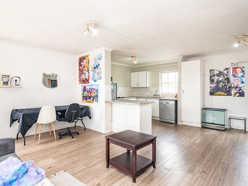 Open-plan living and kitchen area featuring laminate flooring, a breakfast counter, and functional kitchen cabinetry with a built-in pantry.