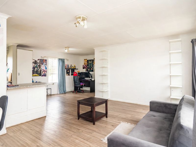 Open plan living area featuring laminate flooring, built-in wall shelving, and a breakfast bar counter, offering a versatile space for living and dining.