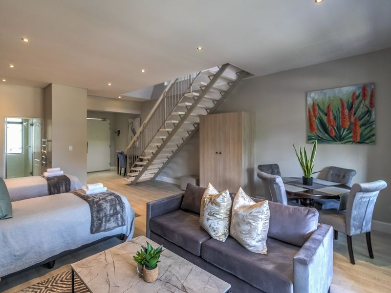 Spacious open-plan living area featuring a modern staircase, neutral finishes, and integrated lighting, creating a versatile and comfortable living space.