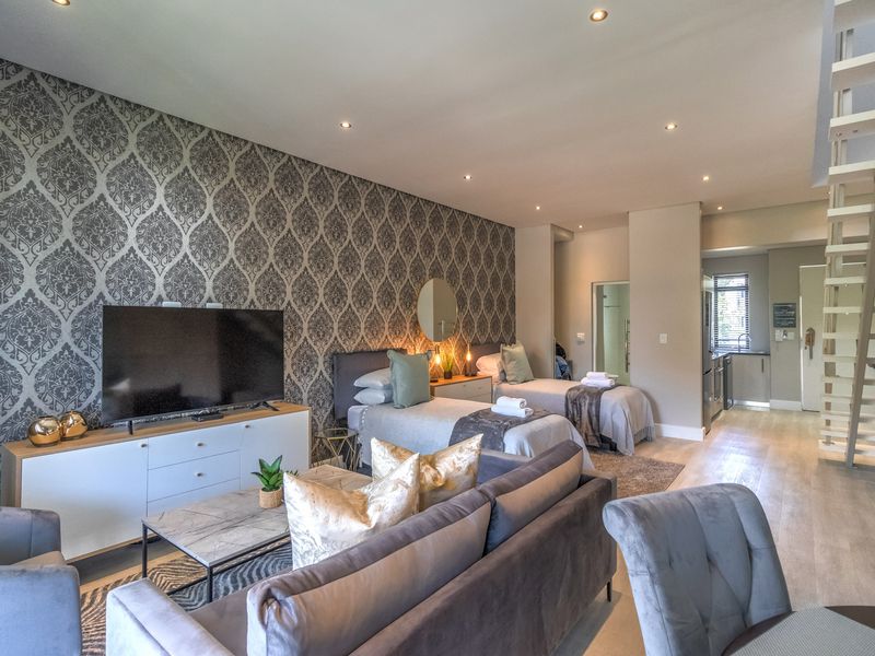 Spacious open-plan living area featuring a bedroom section, modern staircase, recessed lighting, and stylish patterned wallpaper.